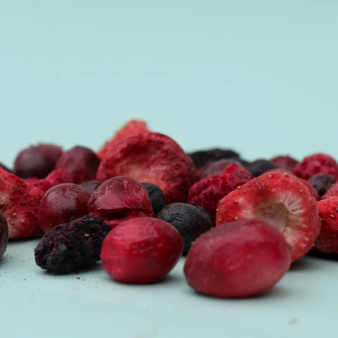 Assorted frozen berries including cranberries and raspberries on a light blue background